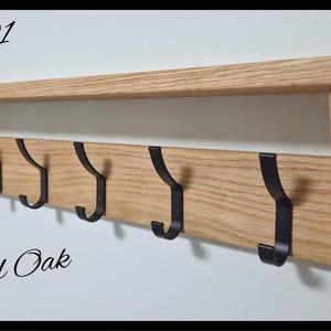 May include: A natural oak wall-mounted shelf featuring six black metal hooks. The wood has a visible grain pattern. Text on the image includes Code 01, Natural Oak, and a circular logo for Nilsa Prairie Handcrafted in Canada.