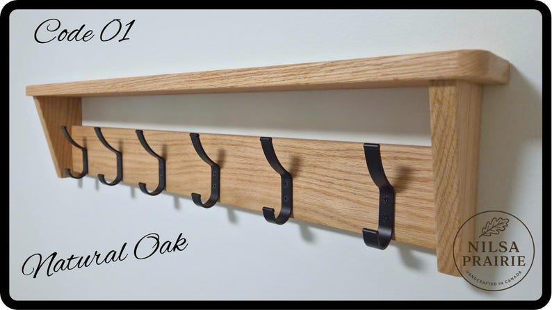 May include: A natural oak wall-mounted shelf featuring six black metal hooks. The wood has a visible grain pattern. Text on the image includes Code 01, Natural Oak, and a circular logo for Nilsa Prairie Handcrafted in Canada.