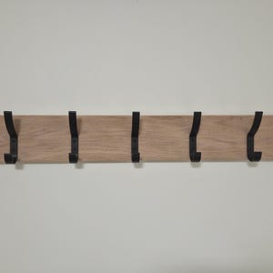 May include: A horizontal rectangular light brown wooden wall rack featuring seven evenly spaced black metal hooks. Each hook is attached to the front of the wooden board, providing a functional storage solution for hanging various items.
