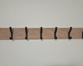 Può includere: Un appendiabiti da parete orizzontale rettangolare in legno marrone chiaro con sette ganci in metallo nero distanziati uniformemente. Ogni gancio è fissato sulla parte anteriore della tavola di legno per appendere vari oggetti.