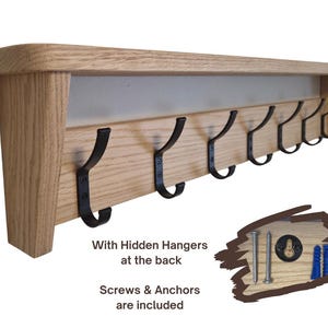 May include: A light-colored wooden wall shelf featuring seven black metal hooks attached to the front panel. The shelf includes hidden hangers at the back, and the set comes with two metal screws and two blue plastic wall anchors for installation.
