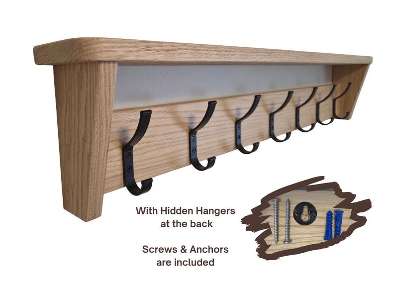May include: A light-colored wooden wall shelf featuring seven black metal hooks attached to the front panel. The shelf includes hidden hangers at the back, and the set comes with two metal screws and two blue plastic wall anchors for installation.