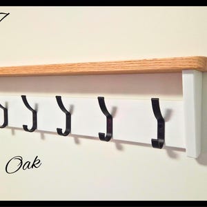 May include: A wall-mounted coat rack featuring a natural oak wood shelf top, a white horizontal backboard, and six black metal hooks. The text Code 17 is in the top left, and a circular logo for NILSA PRAIRIE is in the top right corner.