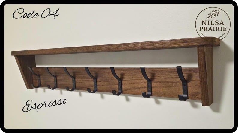 May include: A wall-mounted wooden coat rack with an espresso finish, featuring a top shelf and seven black metal hooks. The text Code 04 and Espresso are printed on the image, along with a circular logo reading NILSA PRAIRIE HANDMADE CANADA.