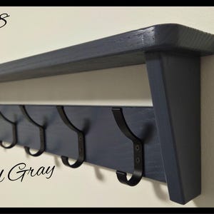 May include: A charcoal gray wooden wall shelf featuring a flat top surface and a lower horizontal board equipped with seven black metal hooks. The text Code 08 and Charcoal Gray are visible, along with a circular logo reading Nilsa Prairie.