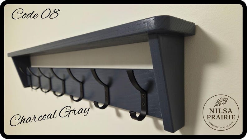 May include: A charcoal gray wooden wall shelf featuring a flat top surface and a lower horizontal board equipped with seven black metal hooks. The text Code 08 and Charcoal Gray are visible, along with a circular logo reading Nilsa Prairie.
