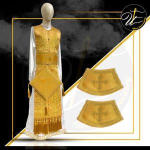 May include: A white liturgical robe featuring a gold vestment with intricate embroidery, a square-shaped piece with a cross, and long gold fringe at the hem. Two matching gold cuffs with cross embroidery are displayed to the right of the mannequin.