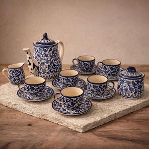 May include: A blue and white floral patterned tea set, including a teapot, creamer, sugar bowl, saucers, and teacups. The teacups and saucers are arranged on a stone surface. The teapot has a curved spout and handle.