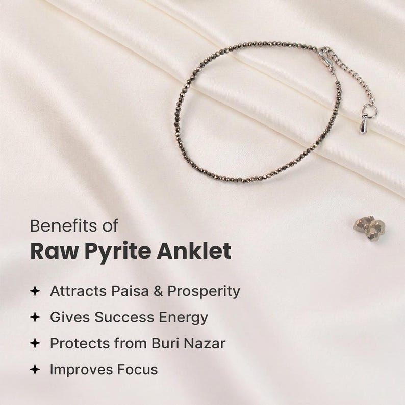 May include: A raw pyrite anklet featuring small, dark grey beads and a silver clasp, presented on a white satin backdrop. The image includes text detailing the anklet's benefits, such as attracting prosperity and enhancing focus.