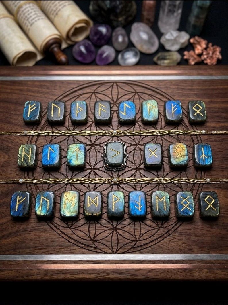 Puede incluir: Piedras r&uacute;nicas de labradorita con s&iacute;mbolos dorados, dispuestas sobre una superficie de madera con un patr&oacute;n decorativo. La imagen incluye un anillo y otros cristales. La disposici&oacute;n resalta los detalles finos de las piedras.