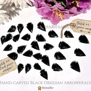 May include: A collection of hand-carved black obsidian arrowheads. Each piece is unique, as indicated by the attached tags. The image includes text that reads "Batch #4 - Each piece unique!" and "Hand-Carved Black Obsidian Arrowheads."