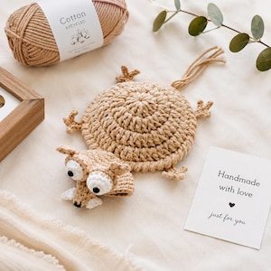 May include: A crocheted frog-shaped coaster and matching frog head, in tan and white. A ball of recycled cotton yarn and a card that reads "Handmade with love just for you" are also in the image. The coaster is approximately 15 cm in diameter.