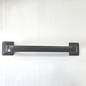 May include: A dark gray metal cabinet pull with a smooth, horizontal bar design and two square-shaped mounting bases on each end. The hardware features a matte finish and a clean, linear structure, providing a functional grip for furniture.