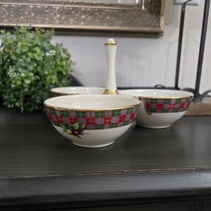 May include: A three-section serving dish with a white handle and three white bowls. The bowls have a red, green, and gray plaid pattern with gold trim. A small floral design is on the side of each bowl.