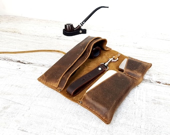 May include: A brown leather tobacco pouch with a zipper closure, a metal hook, and a small pocket. The pouch is open and shows a pipe, a lighter, and a small pouch inside.