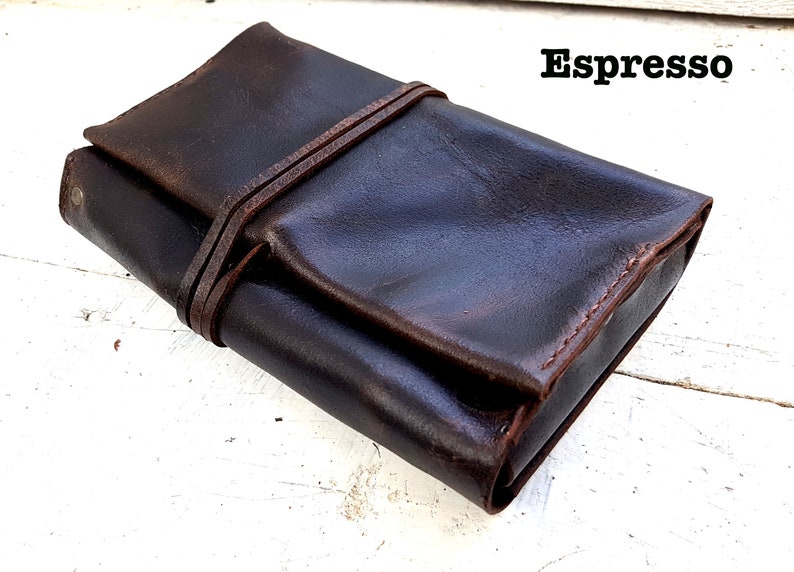 Puede incluir: Un estuche enrollable de cuero marr&oacute;n oscuro con cierre de correa. El estuche est&aacute; hecho de cuero envejecido y tiene un aspecto r&uacute;stico. El texto "Espresso" es visible en la esquina superior derecha de la imagen.