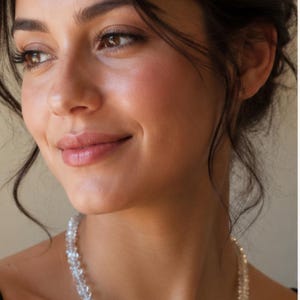 Puede incluir: Se lleva un collar de cristal transparente y facetado. El collar está hecho de pequeños cristales transparentes ensartados. La persona que lleva el collar tiene el pelo oscuro y está sonriendo.