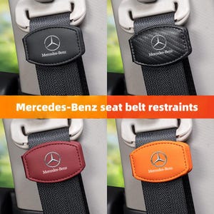 Può includere: Quattro fermi per cinture di sicurezza neri, in fibra di carbonio, bordeaux e arancioni. Ognuno ha un logo e un testo Mercedes-Benz. I fermi sono attaccati a cinture di sicurezza grigie.