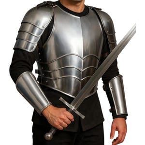 May include: A polished silver metal chest armor with matching shoulder and arm guards. The armor is layered and riveted, with a sword held in the hand. The person is wearing a black long-sleeve shirt.