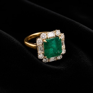 May include: A gold ring featuring a large, rectangular, emerald-cut green gemstone at the center. The center stone is surrounded by a halo of alternating round brilliant-cut diamonds and rectangular baguette-cut diamonds set in a gold band.