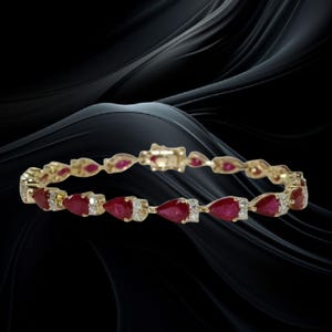 May include: A gold bangle bracelet featuring pear-shaped red gemstones and small white diamonds. The bracelet has a clasp closure and is set against a black background with flowing, dark lines.