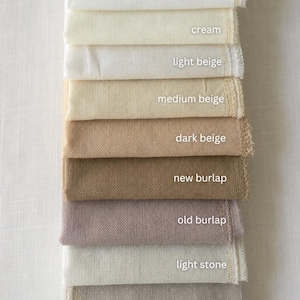 May include: A vertical stack of eleven fabric swatches in various neutral tones. Each swatch is labeled with its color name: white, off-white, cream, light beige, medium beige, dark beige, new burlap, old burlap, light stone, stone, and gray.
