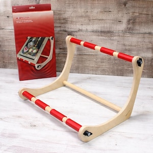 May include: A Nurge brand wooden embroidery lap stand featuring two horizontal bars with red foam padding, connected by curved side supports with black adjustment knobs, accompanied by its original red cardboard packaging box.