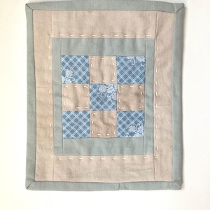 Peut inclure: Une tenture murale rectangulaire en tissu présentant un bloc de courtepointe central à neuf carrés, alternant des carrés à motifs floraux bleus et blancs et des carrés beiges unis. L'ensemble est bordé d'une bordure beige et d'une bordure vert sauge.