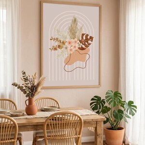 Puede incluir: Una lámina de arte mural enmarcada que presenta un arreglo central de hierba de la pampa seca, eucalipto y hojas de monstera sobre un fondo beige claro con líneas de arco concéntricas blancas y formas orgánicas en tonos tierra.
