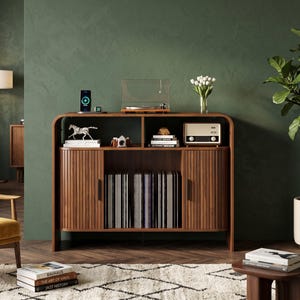 May include: A walnut wood media console featuring rounded edges, two tambour doors, and an open central storage area. The unit holds a record player, a vintage-style radio, books, a small camera, and a collection of vinyl records inside.