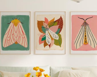 May include: Three rectangular wall art prints featuring moth illustrations. The left print shows a moth on a teal background, the center print displays a moth amidst colorful leaves, and the right print depicts a moth on a pink background.