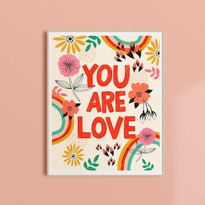 Pu&ograve; includere: Uno sfondo bianco con un arcobaleno colorato e un motivo floreale. Il testo "You Are Love" &egrave; in lettere rosse.