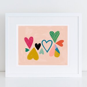 May include: A framed print with a pink background featuring a cluster of colorful hearts. The hearts are in various shapes and sizes, with patterns like stripes and polka dots.