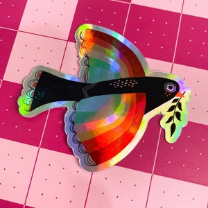 May include: A holographic sticker of a black and white bird with a rainbow wingspan and a green olive branch in its beak.