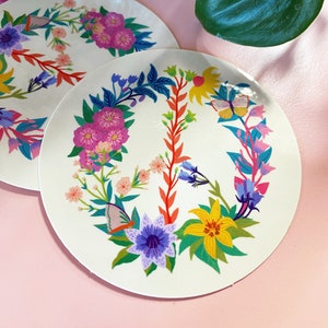 May include: A white round sticker with a peace sign design. The peace sign is made of colorful flowers, leaves, and butterflies. The sticker is perfect for adding a touch of whimsy to any surface.