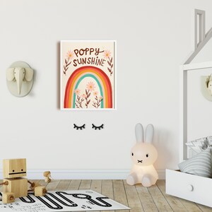 May include: A framed art print with the words "Poppy Sunshine" above a rainbow and flowers. The room features a wooden toy, a bunny lamp, and decorative animal heads on the wall, creating a playful nursery theme.
