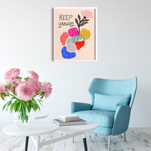 May include: A framed print with a pink background and a black and white illustration of a plant with colorful abstract shapes around it. The text "KEEP GROWING" is written in black cursive.