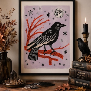 May include: A framed print featuring a black crow perched on a red branch against a light purple background. The artwork includes a white moon and several black stars. The crow is depicted in profile with detailed wing feathers and a sharp beak.