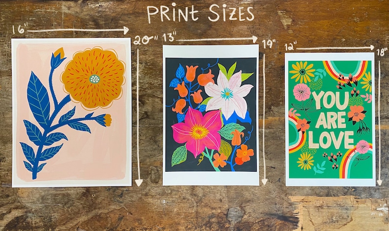 May include: Three rectangular art prints with floral designs. The left print is 16 inches by 20 inches, featuring a yellow flower on a pink background. The middle print is 13 inches by 19 inches, with colorful flowers on black. The right print is 12 inches by 18 inches, green with flowers and the text YOU ARE LOVE.