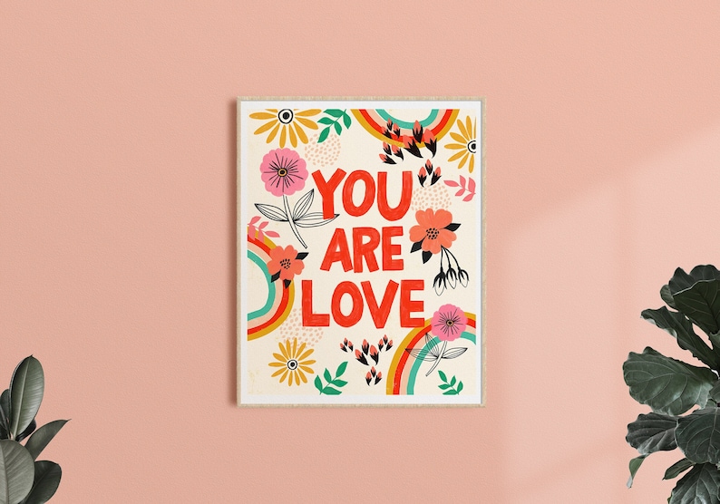 Pu&ograve; includere: Uno sfondo bianco con un arcobaleno colorato e un motivo floreale. Il testo "You Are Love" &egrave; in lettere rosse.