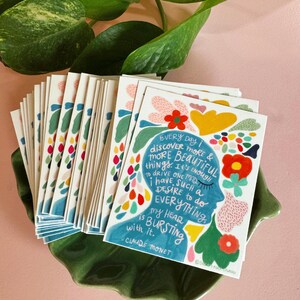 May include: A stack of colorful cards with a quote by Claude Monet. The quote reads "Every day I discover more & more beautiful things. It's enough to drive one mad. I have such a desire to do everything. My heart is bursting with it."