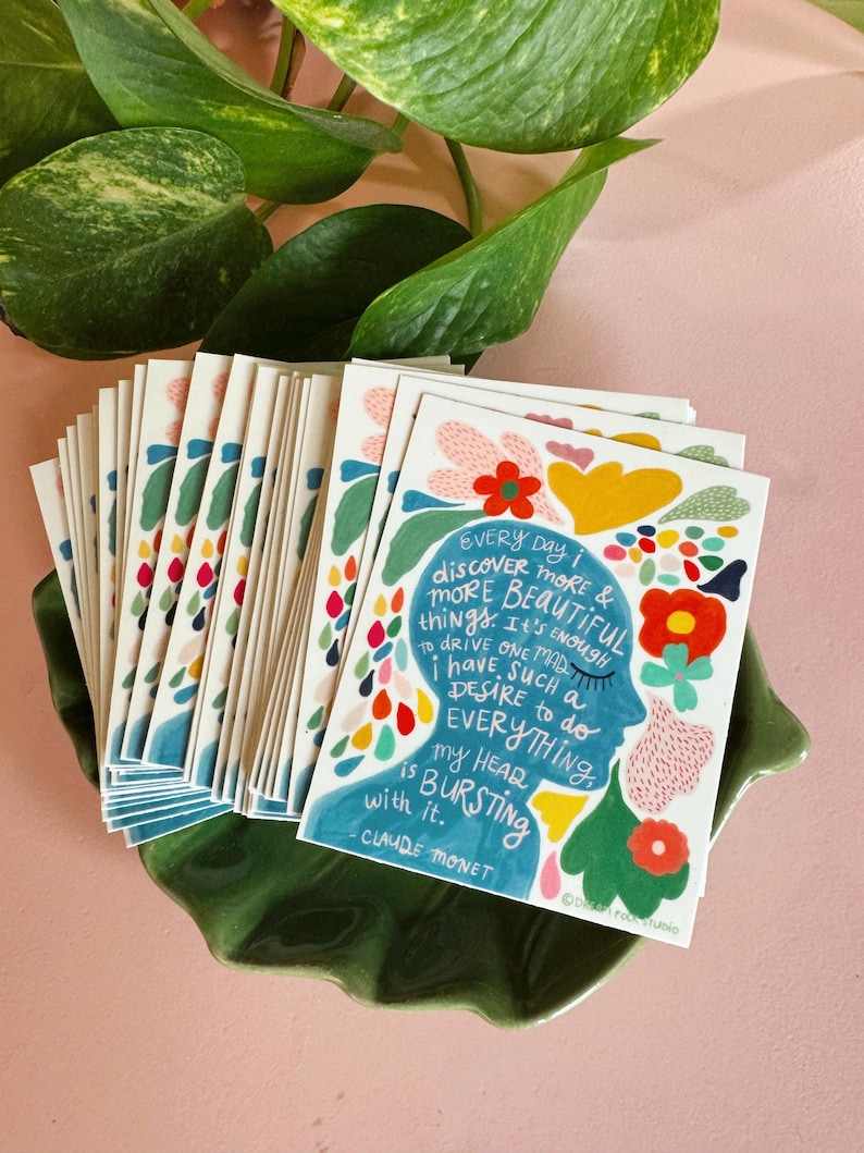 May include: A stack of colorful cards with a quote by Claude Monet. The quote reads "Every day I discover more & more beautiful things. It's enough to drive one mad. I have such a desire to do everything. My heart is bursting with it."