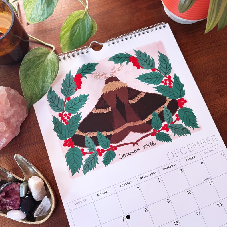 May include: A December moth calendar page featuring a brown and black moth illustration surrounded by green leaves and red berries. The word "December" is at the bottom, with the days of the week listed.