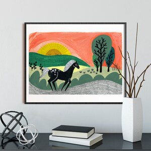 Puede incluir: Un caballo negro con marcas blancas corre por un campo verde con una puesta de sol roja y naranja en el fondo. Hay dos &aacute;rboles verdes en la distancia.