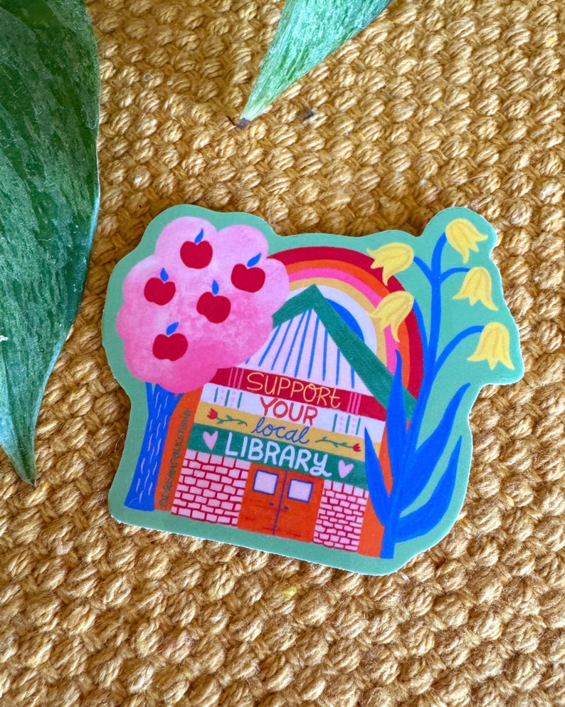 May include: A green sticker with a colorful illustration of a library building with a rainbow, apple tree, and flowers. The text "SUPPORT YOUR local LIBRARY" is written on the building.