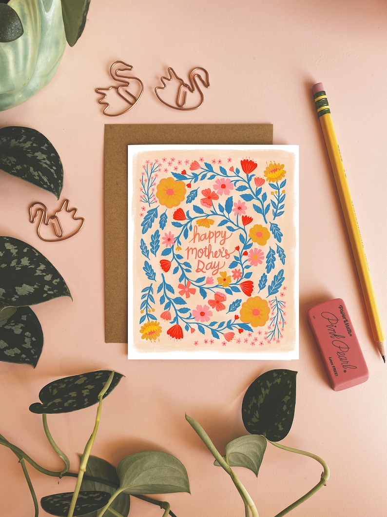 May include: A card with a floral design in shades of pink, yellow, blue, and red. The card has the text 'happy mother's day' in a blue cursive font.