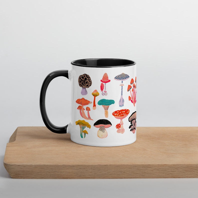 May include: White ceramic mug with a black rim and handle. The mug features a colourful illustration of various types of mushrooms.