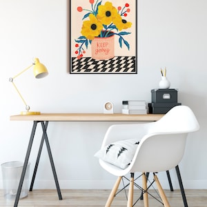 May include: A framed print with a black frame and a white background. The print features a bouquet of yellow flowers in a pink pot with the text "keep going" on the pot. The flowers are on a black and white checkered background.
