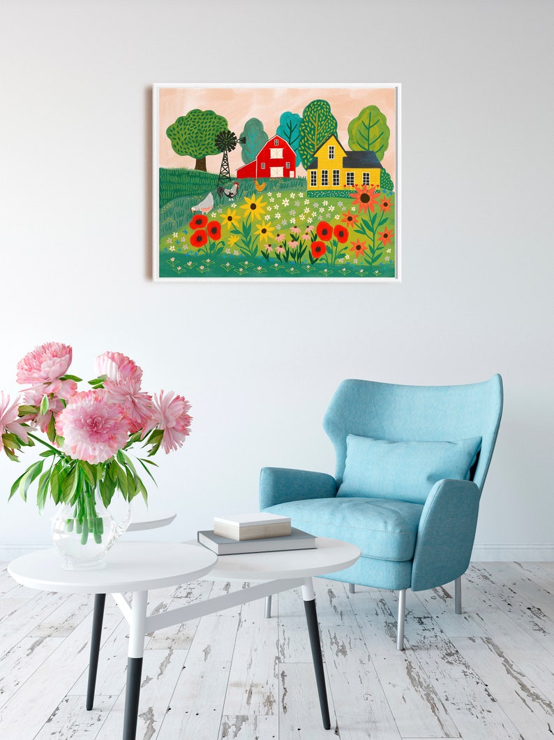 May include: A colorful painting of a red barn and a yellow house in a field of flowers. The painting is framed in white and hangs on a white wall.