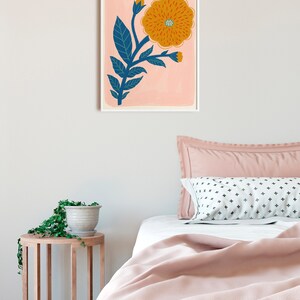 K&ouml;nnte beinhalten: Ein gerahmter Druck einer stilisierten orangefarbenen Blume mit blauen Bl&auml;ttern auf rosa Hintergrund.